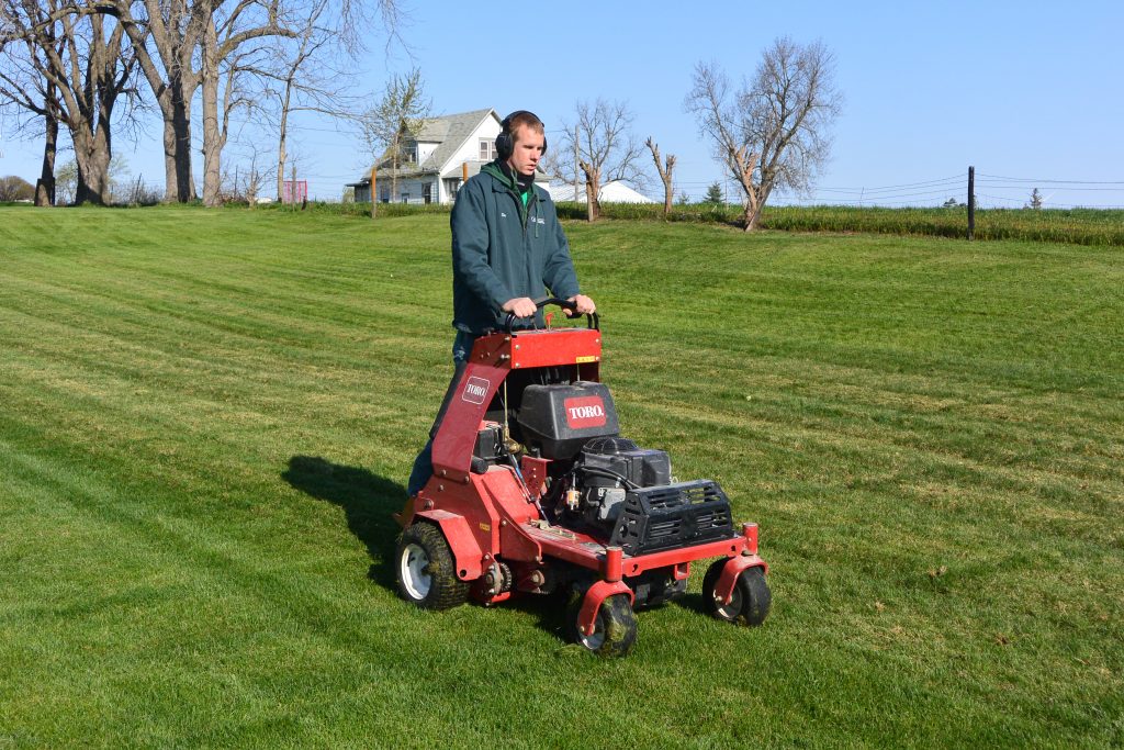 Green Valley employee operating aerator with house in background