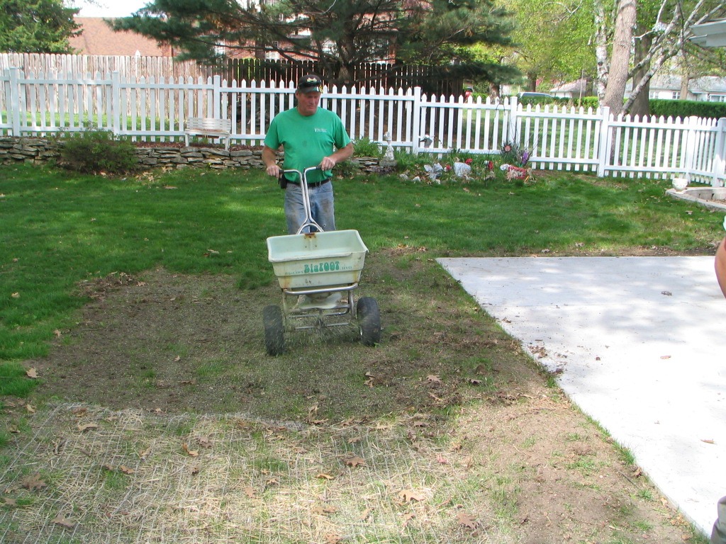 Green Valley employee seeding a lawn with white picket fence in background
