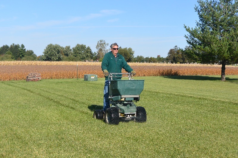 Green Valley employee operating riding fertilizer spreader with cornfield in background