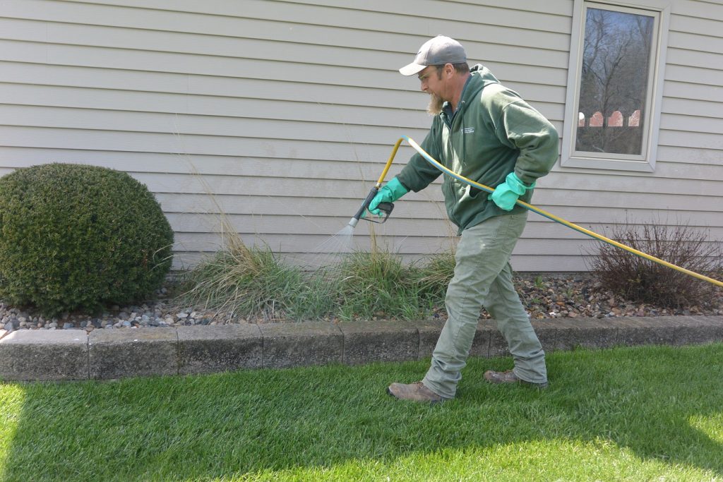 A Green Valley employee spraying the perimeter of a home