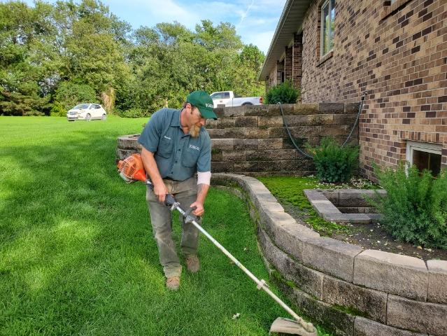 Green Valley employee trimming weeds by garden wall of residence