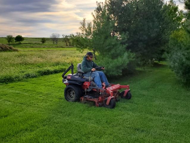 Green Valley employee operating riding mower in lawn with trees